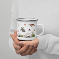 a woman holding a white enamel mug with sea life on it and under the lid