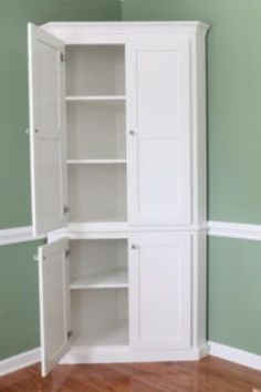 an empty white cabinet in the corner of a room with wood floors and green walls