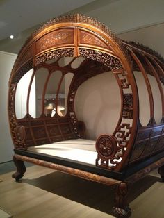 an ornate wooden bed frame on display in a museum exhibit room with white walls and wood flooring