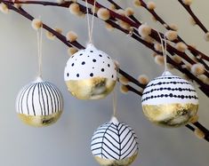 three ornaments hanging from a tree branch in front of a white wall with brown branches