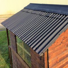 a small wooden building with a metal roof and windows on the side of it, next to a grassy area