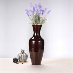 a brown vase with purple flowers in it next to an ornament on a table