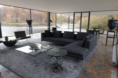 a modern living room with glass walls and floor to ceiling windows looking out onto the water