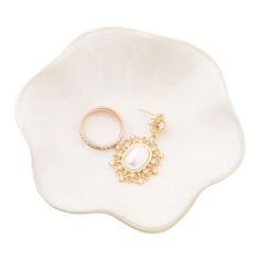 a pair of gold and pearl earrings on a white flower shaped platter with the ring resting on it's side