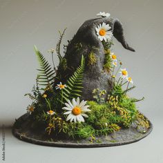 an unusual hat with flowers and ferns on the top is made to look like it's growing out of a rock