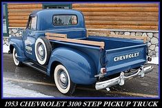 an old blue chevrolet pickup truck parked in front of a log cabin with snow on the ground