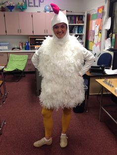 a man dressed in a chicken costume standing next to a desk with chairs and bookshelves