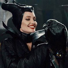 a woman dressed as maleficent holding a black bird in her hand and smiling at the camera