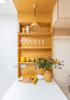 a kitchen with yellow shelves and flowers on the counter