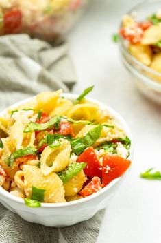 a bowl filled with pasta and vegetables on top of a white table next to another bowl