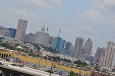 a city skyline with tall buildings in the distance and cars parked on the side of the road