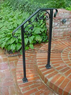 an iron hand rail on the side of a brick wall with green plants in the background