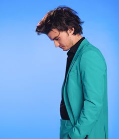 a man in a green suit looking down at his cell phone while standing against a blue background