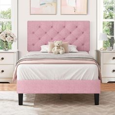 a pink bed with two pictures above it and a teddy bear sitting on the pillow