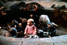 a baby sitting on the ground surrounded by stuffed animals and other animal heads in a circle