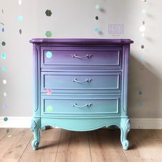 a blue and purple dresser with confetti on the wall behind it in a room