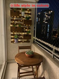 a small table and chair on a balcony with lights in the city behind it at night