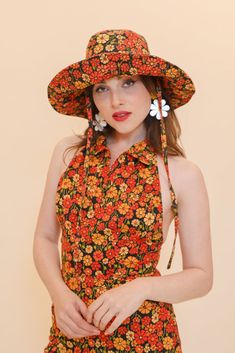 a woman wearing a floral dress and large hat with flowers on it's brim