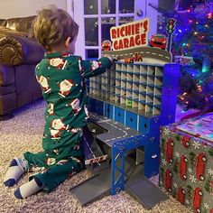 a little boy in pajamas playing with a toy garage next to a christmas tree and presents