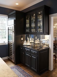 a kitchen with black cabinets and glassware on the counter top in front of a window