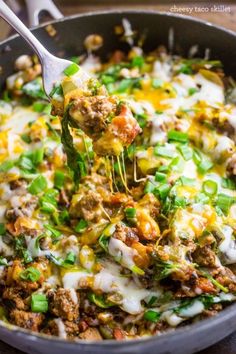 a skillet filled with meat, cheese and green onions being held by a fork