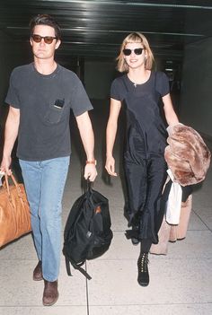 a man and woman walking through an airport carrying luggage