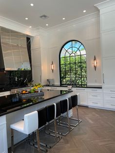 a large kitchen with black counter tops and white chairs in front of an arched window