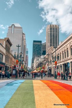 people are walking down the street with buildings in the backgroung and rainbow painted on the sidewalk