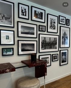 a wall with many pictures on it and a stool in front of the photo display