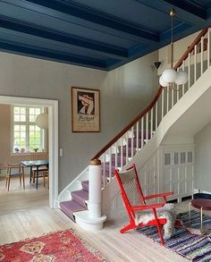 a red chair sitting on top of a wooden floor next to a stair case in a living room