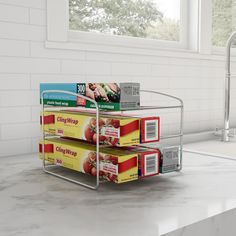 three boxes of food are stacked up on a rack in front of a sink and window