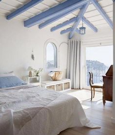 a bedroom with white walls and blue painted beams on the ceiling, along with a large bed