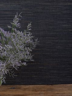 a vase filled with purple flowers sitting on top of a wooden table next to a black wall