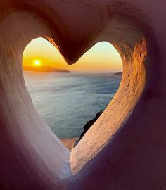 the sun is setting behind a heart - shaped window in an ice cave overlooking the ocean