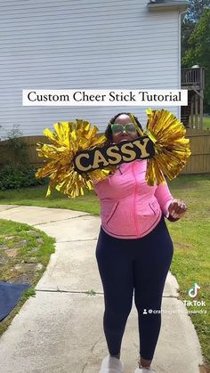 a woman in pink shirt and black leggings holding up a yellow cheer stick