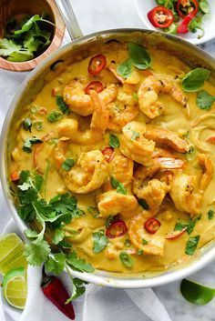 a pan filled with shrimp and sauce next to cilantro, lime wedges