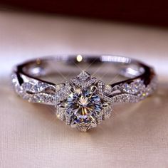 a diamond ring is sitting on top of a white cloth with the center stone surrounded by smaller diamonds