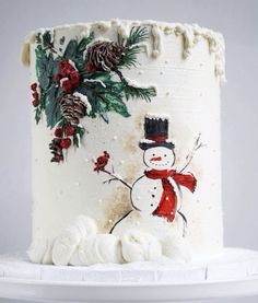 a white frosted cake decorated with a snowman and pine cones