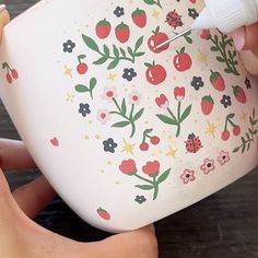 someone is painting the inside of a cup with flowers and ladybugs on it