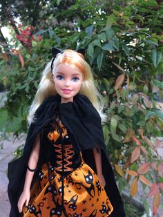 a doll dressed up as a witch standing in front of a bush with leaves on it