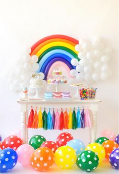 a rainbow themed party with balloons, streamers and cake on a table in the background