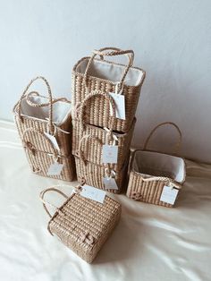 four wicker baskets with tags on them sitting on a white sheeted bed,