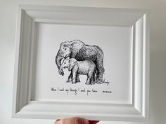 a drawing of an elephant and its baby is shown in a white frame with a hand holding it