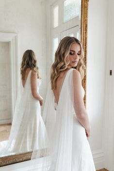 a woman in a white wedding dress looking at her reflection in the mirror while wearing a veil