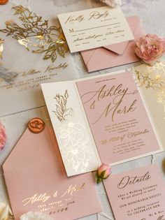 pink and gold wedding stationery with matching envelopes, cards, and flowers on the table