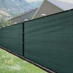 a green privacy fence in front of a house with mountains in the backround