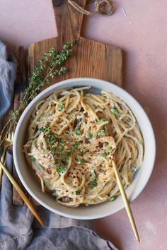 a white bowl filled with pasta on top of a wooden cutting board next to two chopsticks