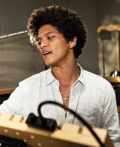 a young man sitting in front of a keyboard and microphone with an instrument behind him