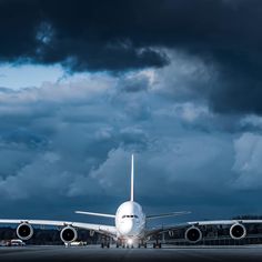 an airplane is sitting on the tarmac under a dark sky with fluffy white clouds