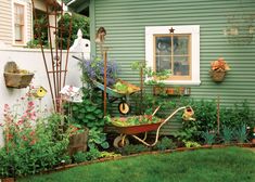 a wheelbarrow filled with lots of plants next to a green house and white fence